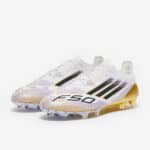 حذاء كرة قدم أديداس F50 Elite FG، تصميم أبيض مع لمسات بنية وذهبية، مثالي للمباريات على الأرض الصلبة.