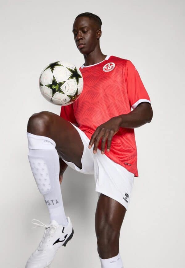Football player performing skill move with ball on knee, wearing team kit.