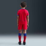 Young boy wearing PSG third kit for kids 2025/26, featuring red and blue colors.