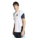 Male model wearing a white soccer jersey with light blue accents and dark sleeves, displaying a team crest on the chest (athletic apparel)