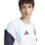 Portrait of a young man wearing a white and light-blue soccer jersey with an Adidas logo and crest, facing slightly left.