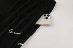 Black Nike Dri-Fit tracksuit with white logo detail, shown with a smartphone tucked into the waistba.