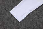 Close-up of white Adidas tracksuit sleeve on textured gray background.