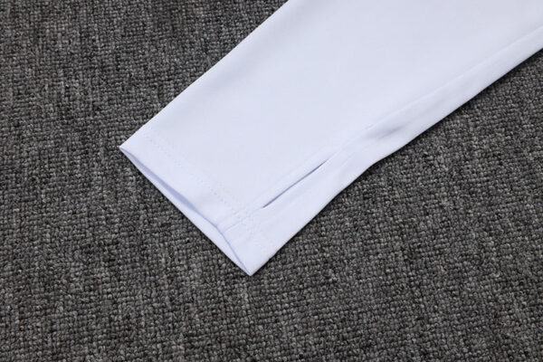 Close-up of white Adidas tracksuit sleeve on textured gray background.
