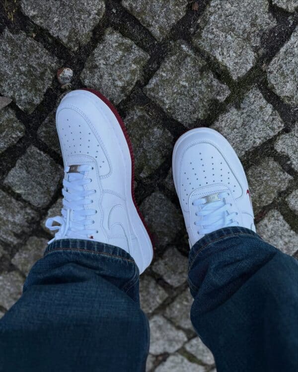 Air Force Low 1 “White/Team Red” sneakers on cobblestone surface.