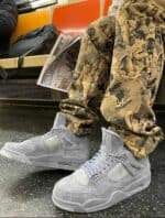 KAWS × Air Jordan 4 Retro 'Cool Grey' sneakers in a subway setting, showcasing stylish footwear.