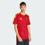 Young man wearing a red Belgium national team jersey, facing the camera with a neutral expression, light gray background