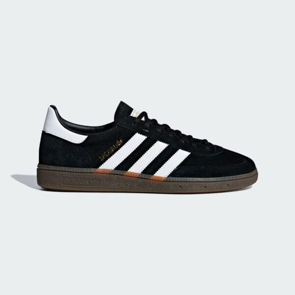 Close-up of a black Adidas sneaker with white three stripes and brown sole, shown from a low angle against a light gray background