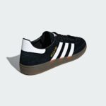Close-up of a black Adidas sneaker with white stripes on a light gray background.
