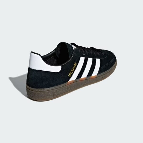 Close-up of a black Adidas sneaker with white stripes on a light gray background.
