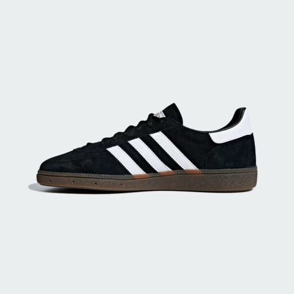 Black Adidas-style sneaker with white stripes on a light gray background (partial view).
