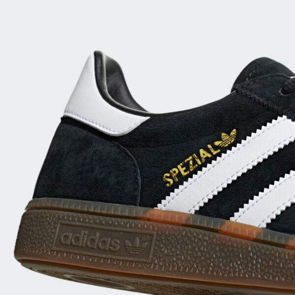 Close-up of a black suede Adidas Spezial sneaker with a white heel trim and gold trefoil logo on the side.