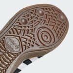 Close-up of a brown rubber shoe sole with intricate circular and geometric tread patterns, showing grip details near the heel area.