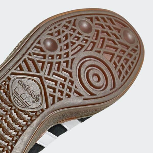 Close-up of a brown rubber shoe sole with intricate circular and geometric tread patterns, showing grip details near the heel area.