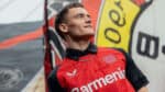 Young male athlete wearing Bayer Leverkusen 2024/25 home football jersey outdoors.