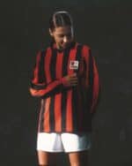 Football jersey with red and black vertical stripes, featuring a crest on the chest.
