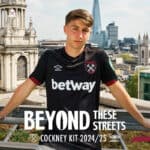 Young male model wearing West Ham United football jersey on rooftop with London skyline.