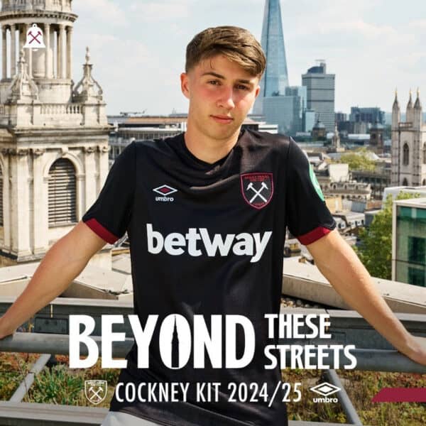 Young male model wearing West Ham United football jersey on rooftop with London skyline.