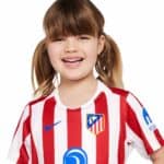 Atletico Madrid kids home football kit for 2025/26 season, featuring red and white vertical stripes,.