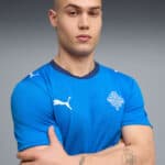 Portrait of a man in a blue athletic shirt with a white Puma logo and crest, arms crossed.