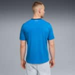 Back view of a man in a bright blue short-sleeve shirt, standing against a gray gradient background.