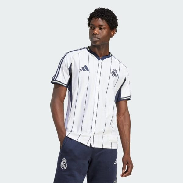 Male model wearing a white Real Madrid football jersey with navy pinstripes, standing against a light gray background.