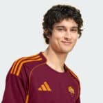 Close-up of a smiling person wearing a maroon Roma football jersey with orange stripes.
