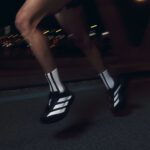 حذاء رياضي أديداس أديزيرو إيفو إس إل باللون الأسود مع خطوط بيضاء، مثالي للجري والتمارين الرياضية.