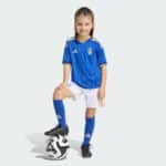 Smiling young girl in a blue Italy soccer jersey with a ball under her foot against a light background.