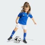 Young girl in Italy soccer kit kicking a black-and-white football on a light background.