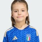 Close-up portrait of a young girl with brown hair and a blue Italy football jersey, smiling softly into the camera.