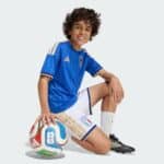 Happy boy in an Italy national team jersey posing with a soccer ball on the ground.