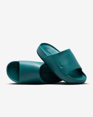 Teal slide sandals stacked on a white background, close-up view of the textured footbed and strap edges.