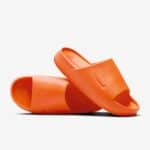 Two bright orange slide sandals with ribbed footbeds placed on a white background, overlapping in a diagonal arrangement.