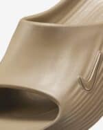 Close-up of a beige shoe upper with a curved edge and a metal hook detail on the side.