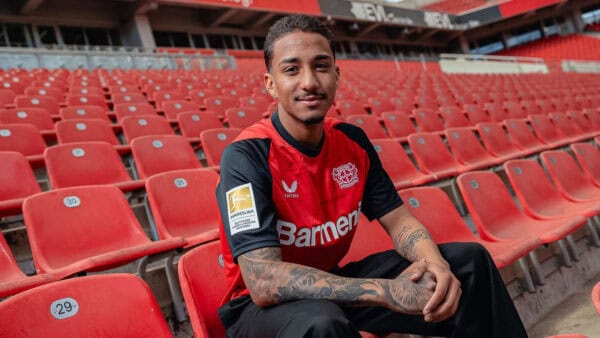 Bayer Leverkusen 2024/25 home football jersey on a model in stadium seats.