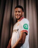 Athletic soccer player in white jersey with green and gold accents, smiling confidently.