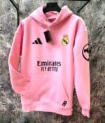 Pink Real Madrid hoodie with club crest, Adidas logo, and "Fly Better" slogan, perfect for football.