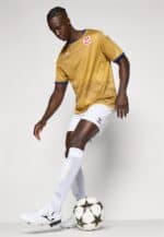 Male football player in gold jersey and white shorts with a soccer ball.