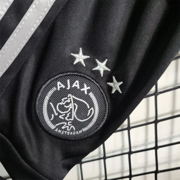 Official Ajax youth football kit for 2023/24 season. Black design with Ajax logo and star details.