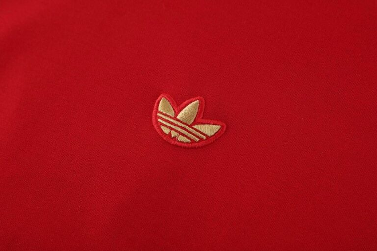 Red Adidas hoodie with gold trefoil logo, sporty casual wear for athletes and fans.