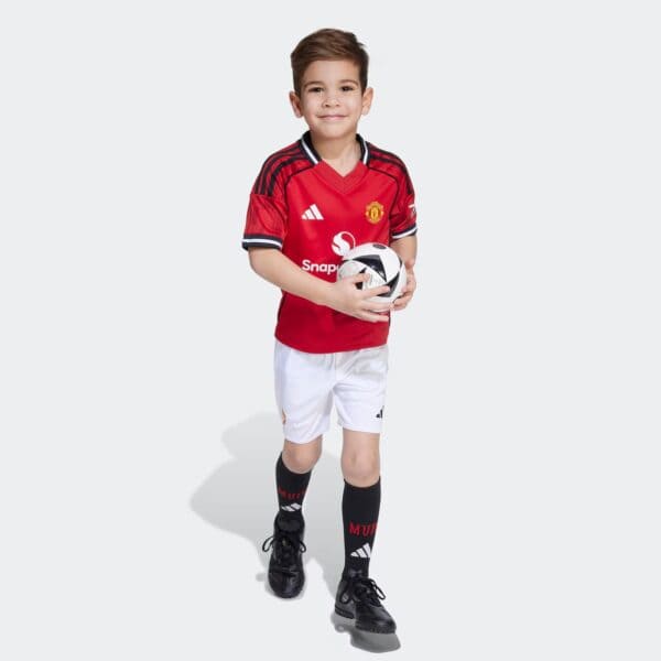 Young boy wearing Manchester United kids home football kit holding a soccer ball.