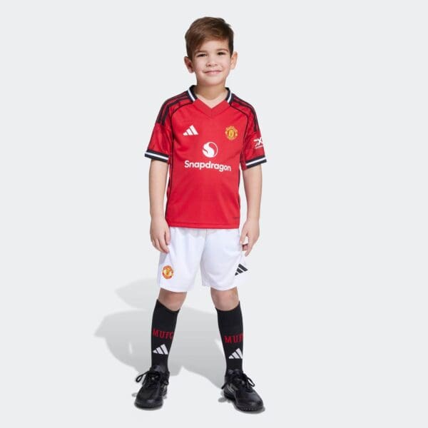 Manchester United kids home football kit, 2025/26 season, featuring red jersey, white shorts, and bl.
