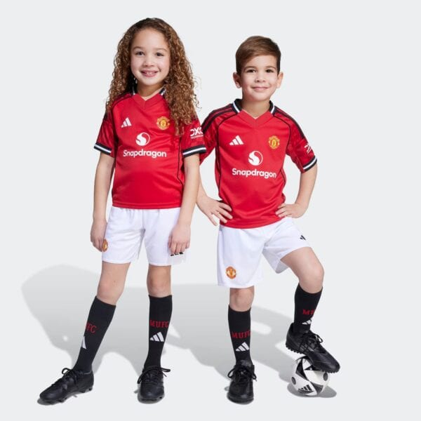 Kids Manchester United home football kit 2025/26, featuring red jersey and white shorts.