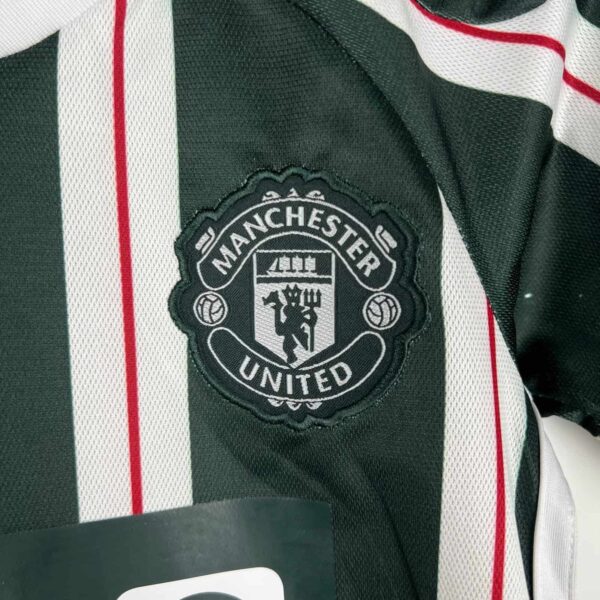 Official Manchester United away kit for kids 2023/24 season featuring club crest.
