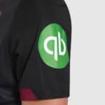 Close-up of black football jersey with green QB logo on sleeve.