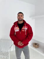Man wearing red F1-inspired racing padded oversized hoodie in a minimal white room.