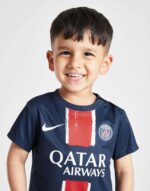 Young boy wearing PSG home football kit 2024/25 for kids, featuring club logo and Qatar Airways spon.