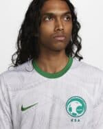 Player wearing KSA SAFF football jersey, front view, white with green accents, Nike logo, and SAFF e.