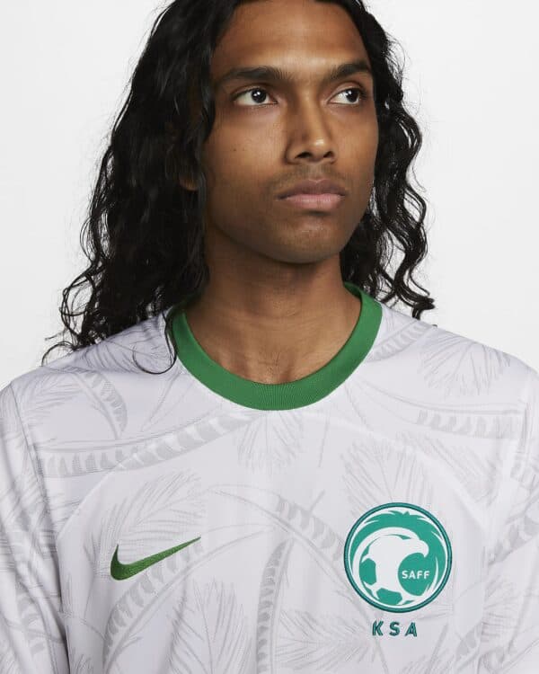 Player wearing KSA SAFF football jersey, front view, white with green accents, Nike logo, and SAFF e.